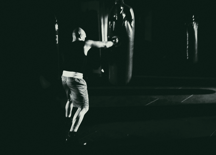 Black and white image of a man punching a punching bag from behind