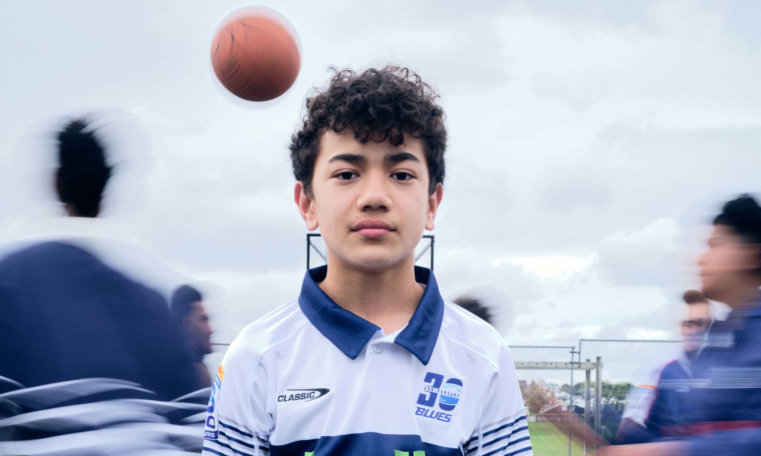 A boy wearing the blues jersey with people playing basketball around him