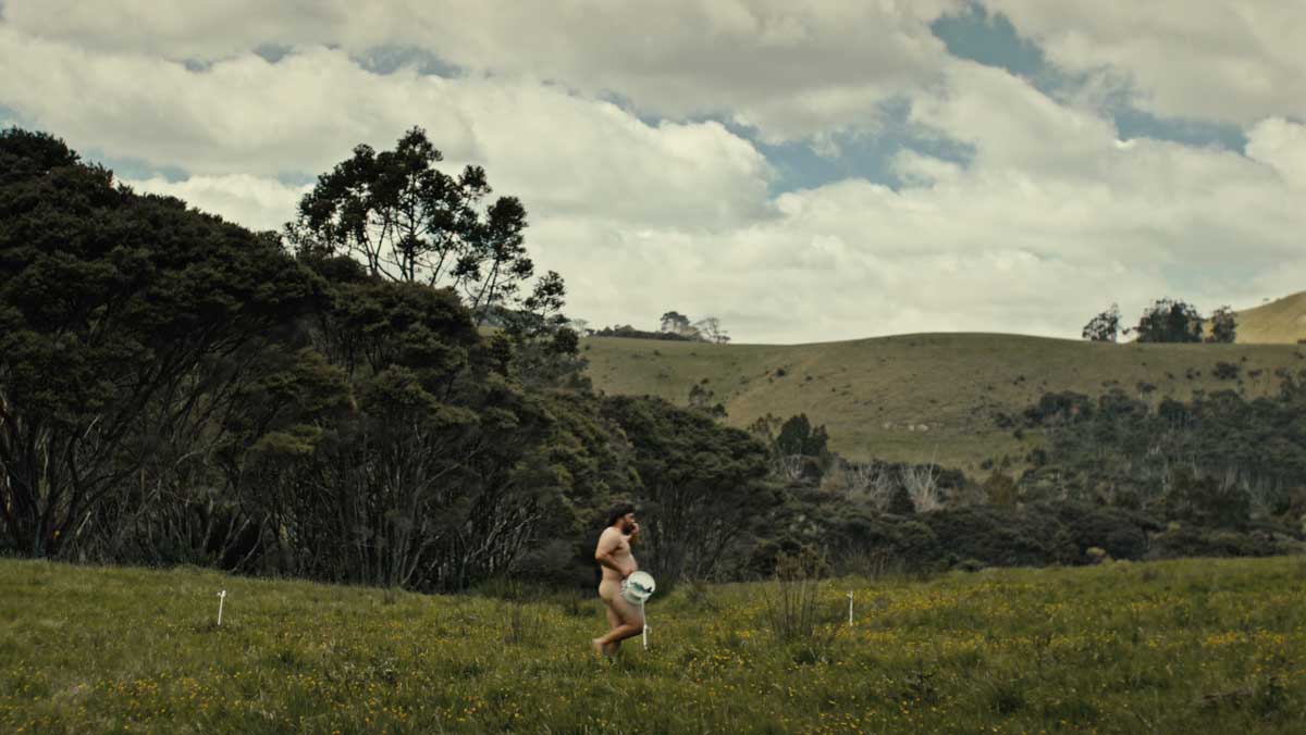 Man walking across a paddock with a reel of electric tape wire covering him