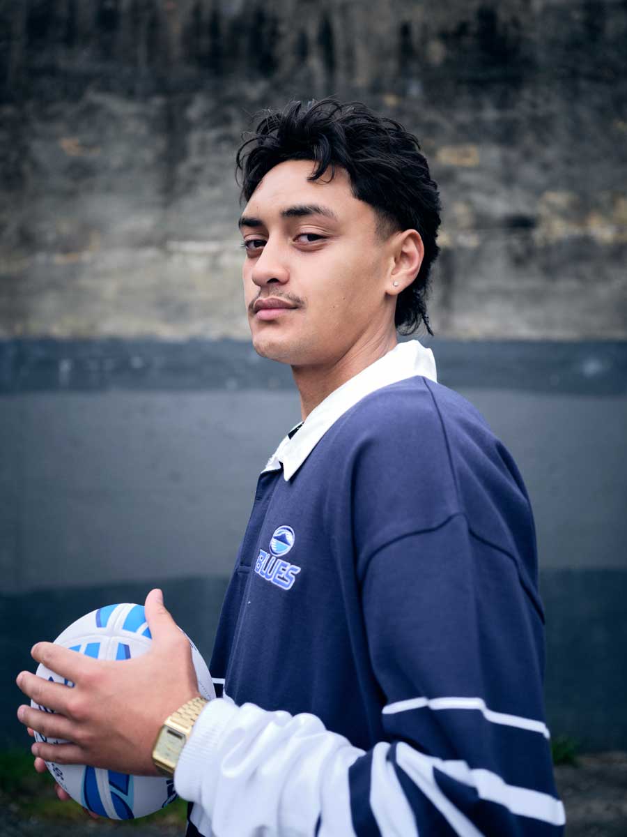 A boy holding a rugby ball in a blues long-sleeved collared shirt