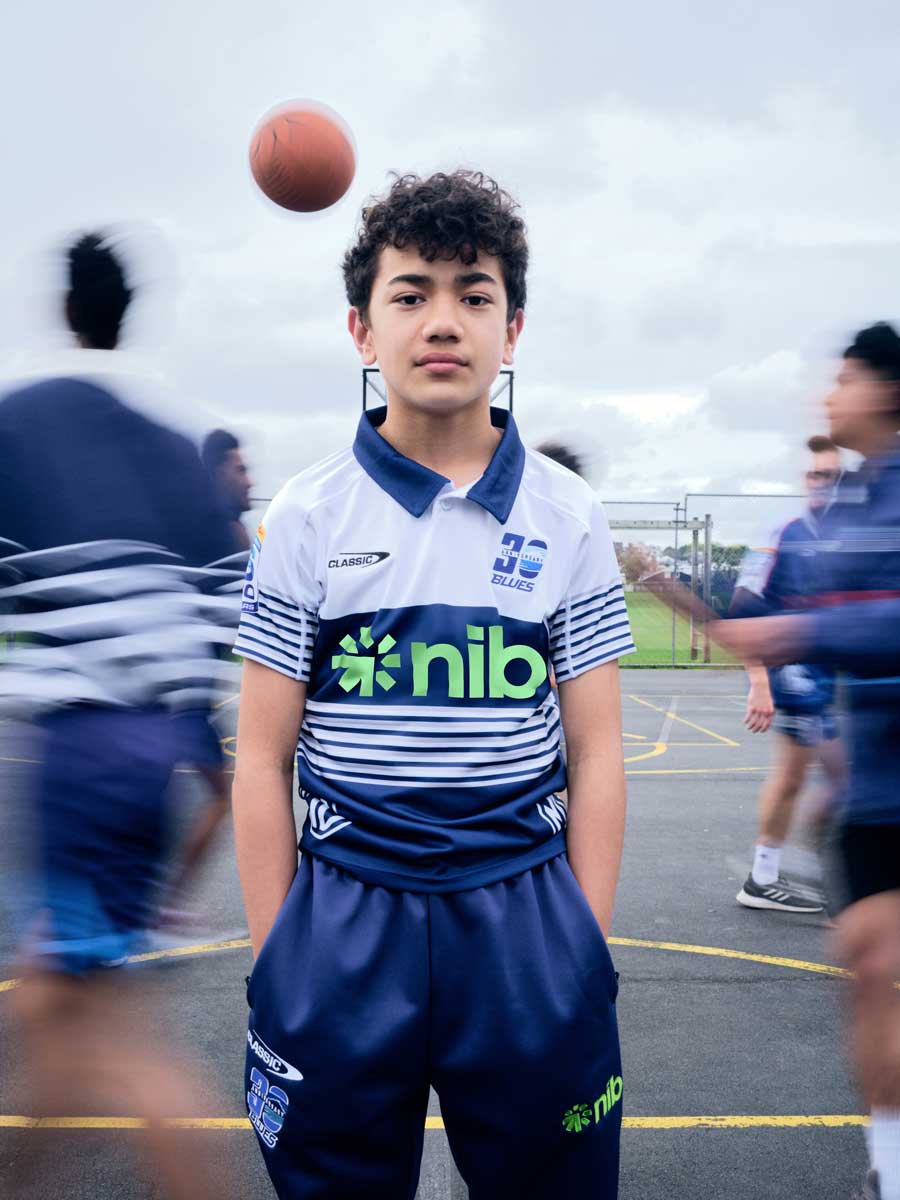 A boy wearing the blues jersey with people playing basketball around him