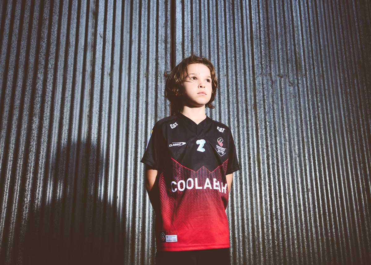 A boy standing in front of raw corrugated steel wearing a crusaders jersey