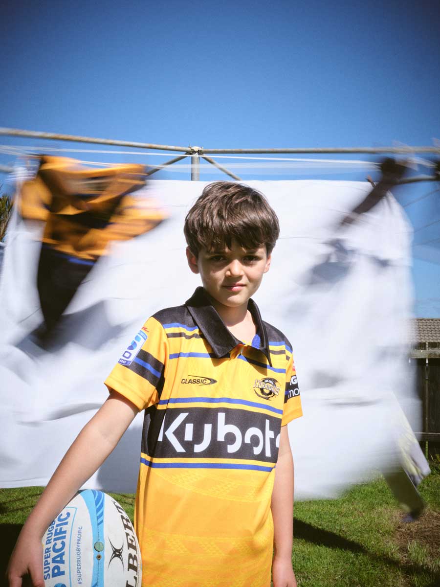 Boy wearing the hurricanes jersey holding a rugby ball in front of a spinning clothesline